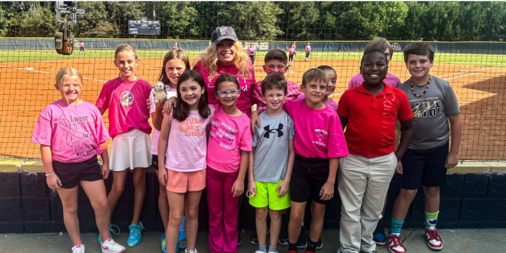 Carol Cheney (center) is surrounded by former and current students as they showed their support of Cheney during Loganville Christian Academy’s “Pink Out” middle school softball game.