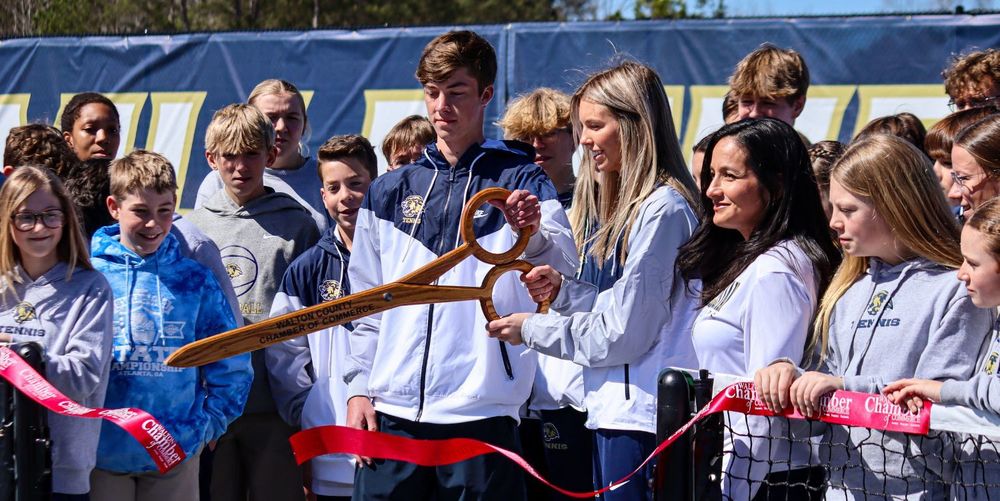 Group of students cutting a ribbon with large scissors