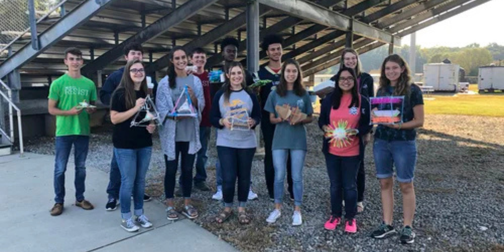 A group of high school students pose for a photo smiling with their eggs for a physics assignment.