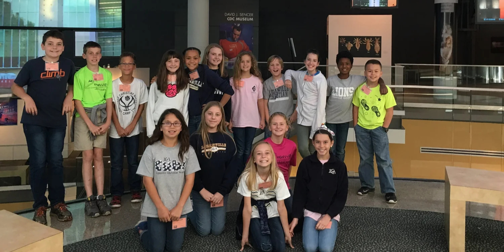 A group of middle school students stand side by side smiling and posing for a photo.