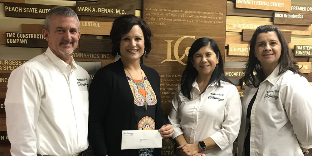 A man (far left) and three women pose for a photo smiling. One woman is holding a white envelope. 