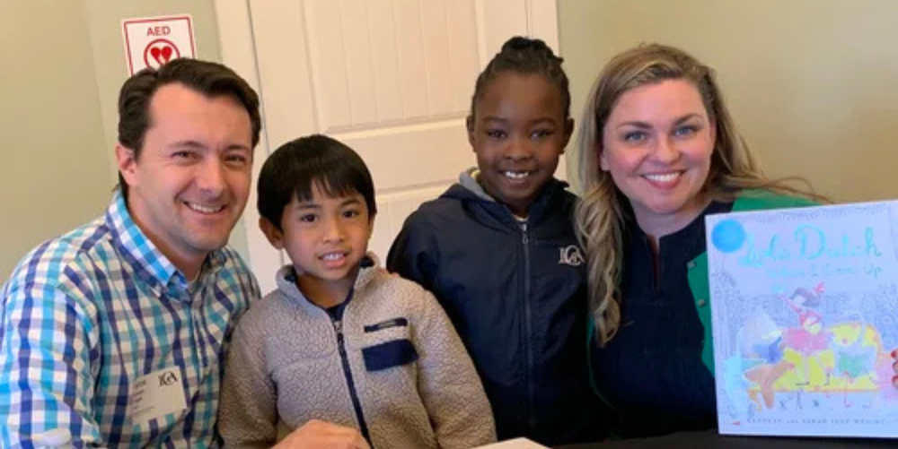 Two adults pose for a photo with two young, school aged children after signing their books.