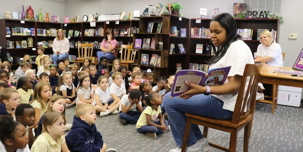Female student reading to young class in library