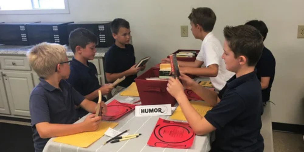 A group of male students gather around one table browsing through a red box of books.