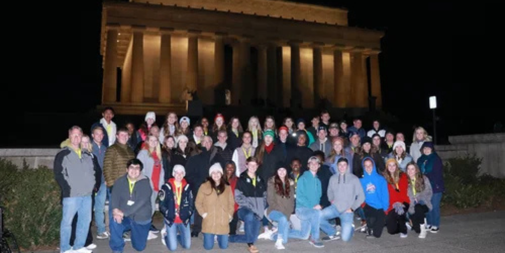 A group of students and staff pose for a photo in front of a large, white building in Washington DC.
