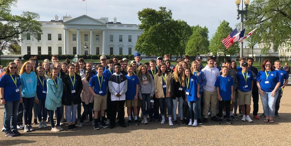 A large group of middle school age students and their teachers pose for a photo in front of The White House. 