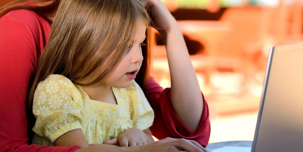A young, brown haired girl sits in front of a laptop working on a project. 