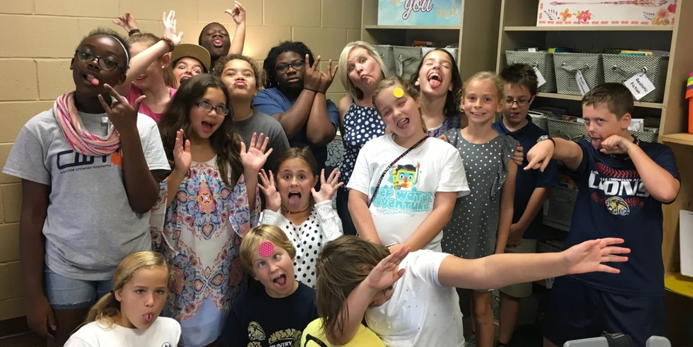 A group of lower school aged students pose for a photo while making goofy looking faces and laughing with each other. 