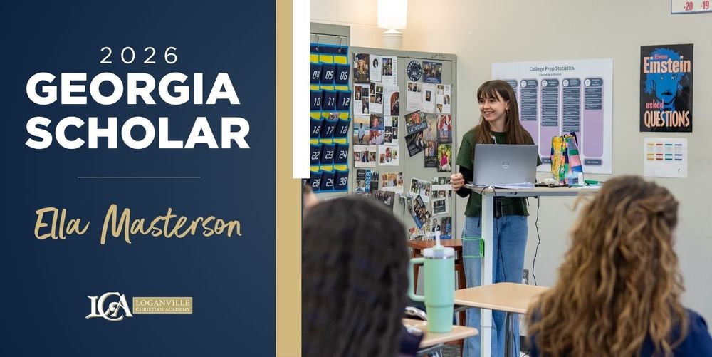 A brown haired girl stands in front of the class smiling while presenting a project to her classmates. 