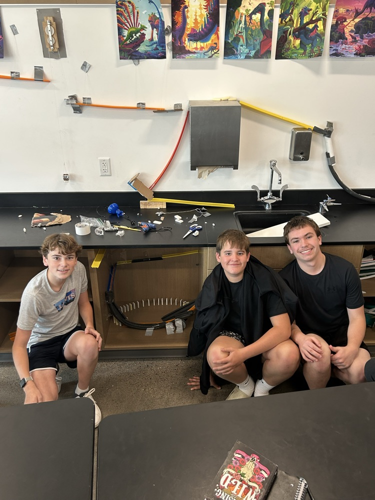 Three students pose with their Rube Goldberg machine before testing to see if it works.