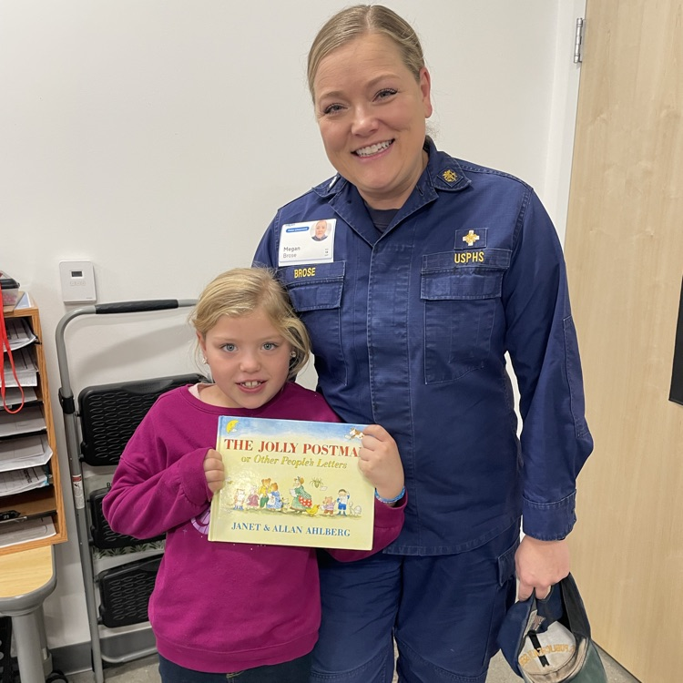 A student stands with her mom, holding the book The Jolly Postman