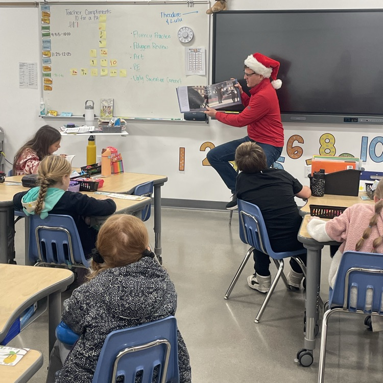 A man in a Santa hat reads to a class 