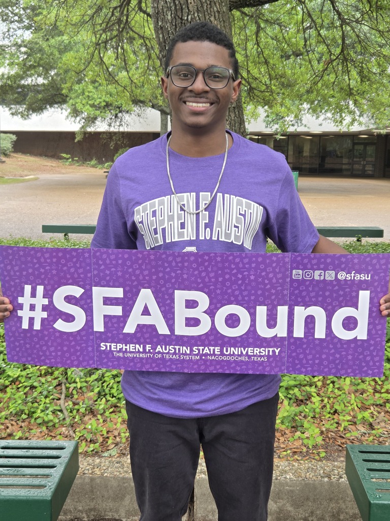Jaylen is wearing his purple SFA shirt and holding a large SFA Bound banner.