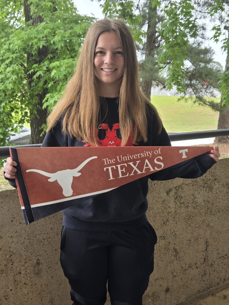 Sophie outside with trees in the background wearing black and holding a University of Texas pennant.