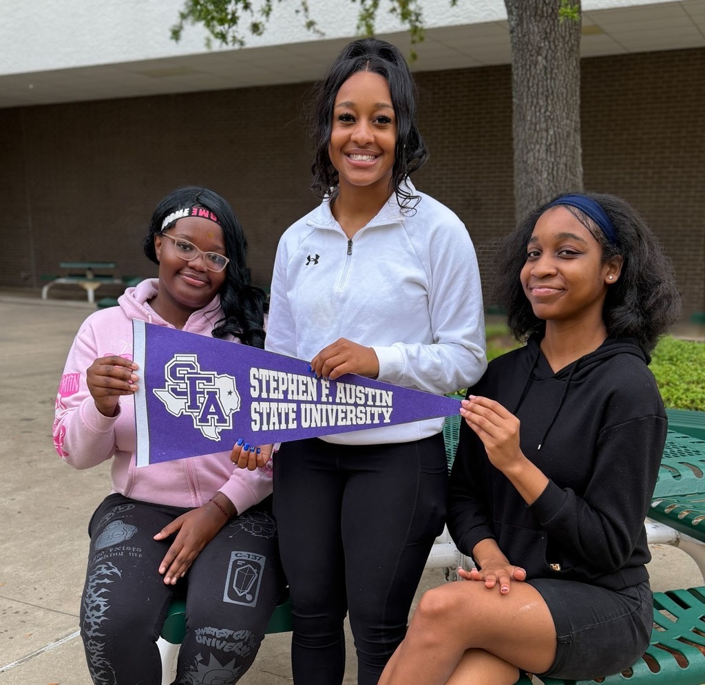 Three girls outside holding a SFA pennant