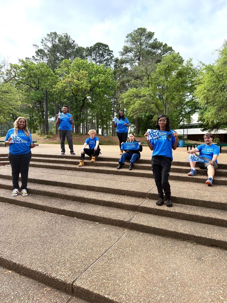 6 students sitting and standing outside wearing Kilgore College shirts and holding pennants.