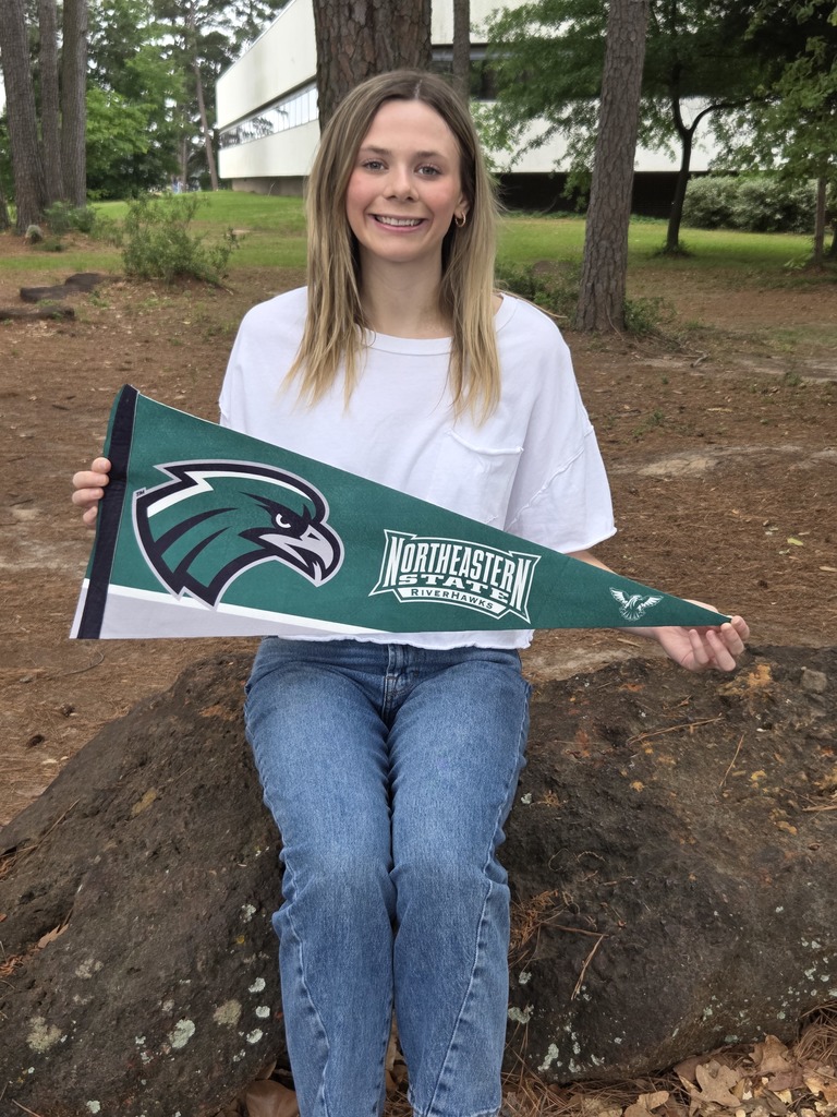 Avery is wearing a white shirt holding a green, grey, and white pennant for Northeastern State University.
