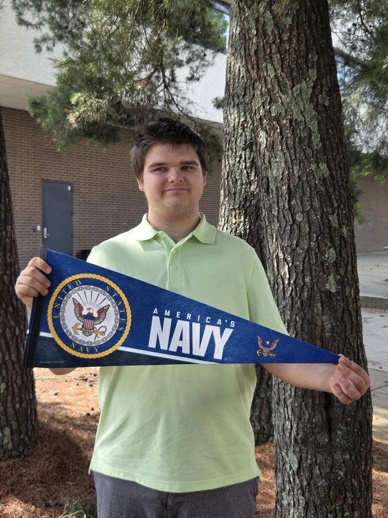 Keith is standing outside wearing a lighted colored polo holding a US Navy pennant