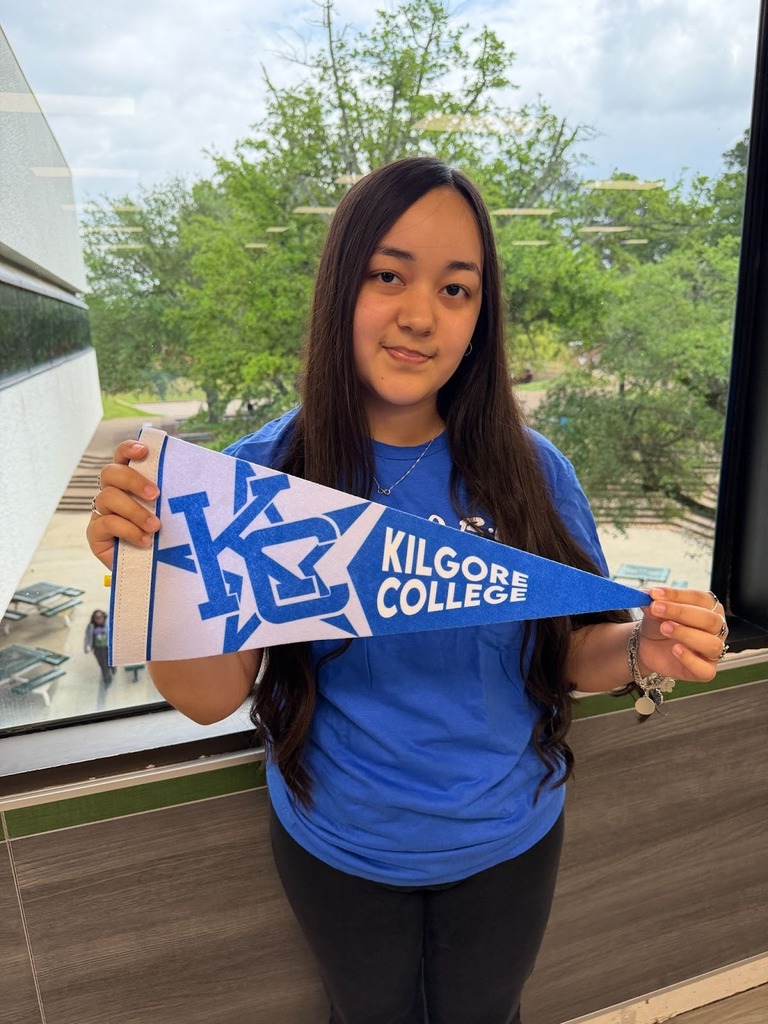 Dennise standing in front of a window holding a Kilgore College pennant