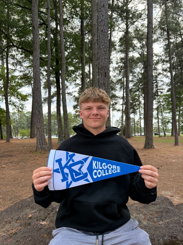 Kayden is sitting on a boulder holding a Kilgore college pennant