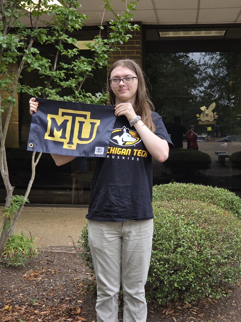 Bryn is holding a MTU banner and wearing a Michgian Tech University shirt