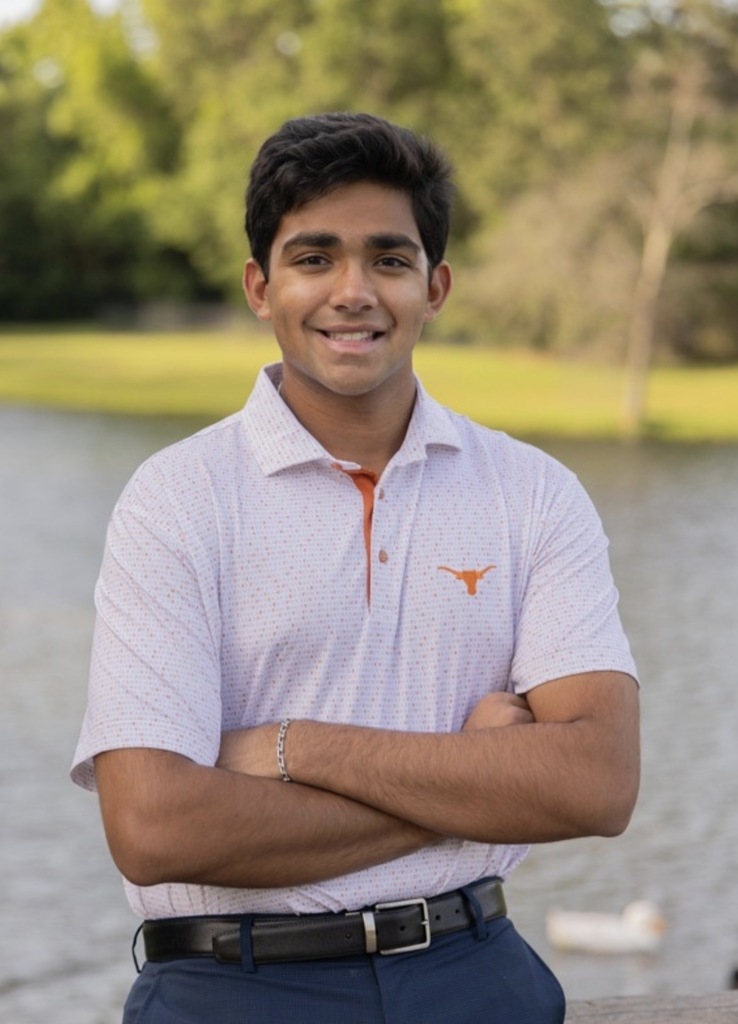 Aarush standing in front of a body of water such as a lake wear in a University of Texas at Austin Polo shirt.