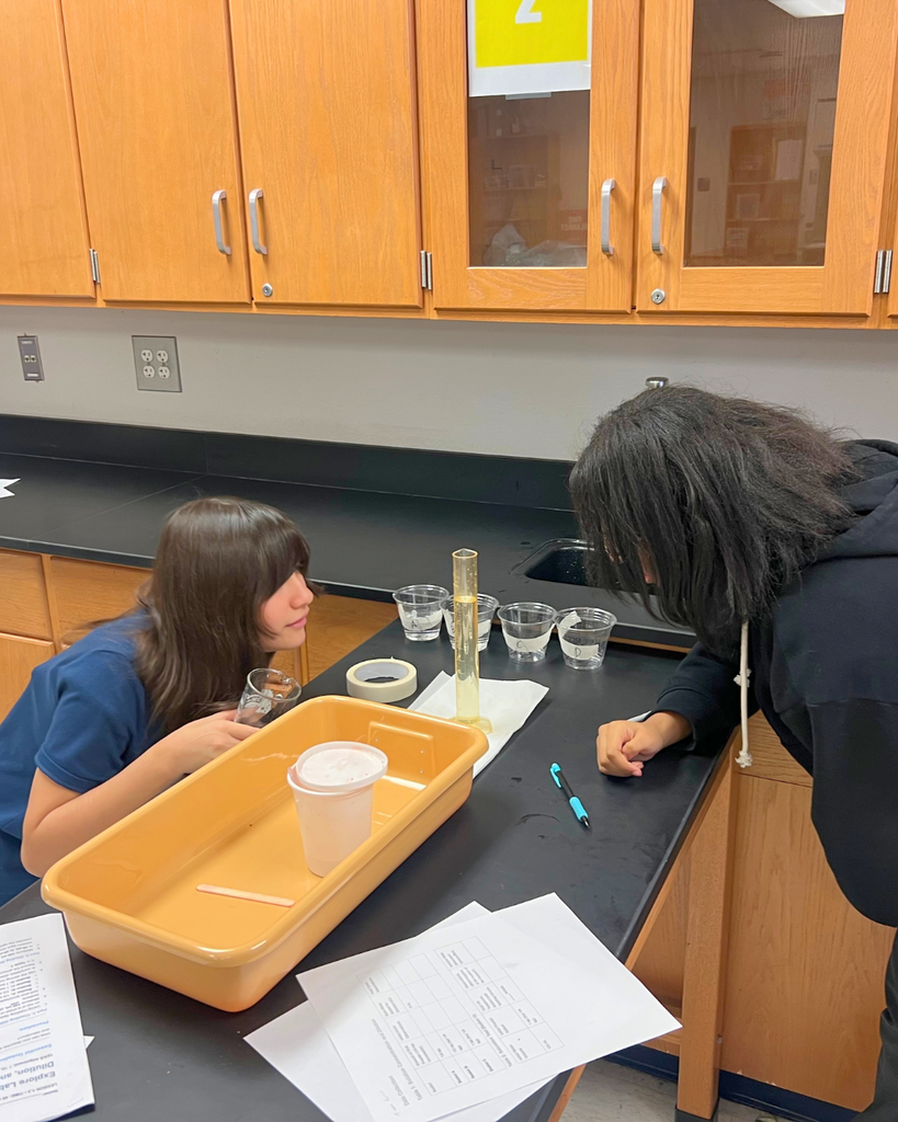 Two middle school students in a science lab performing an experiment at a lab table with beakers and a plastic tub.