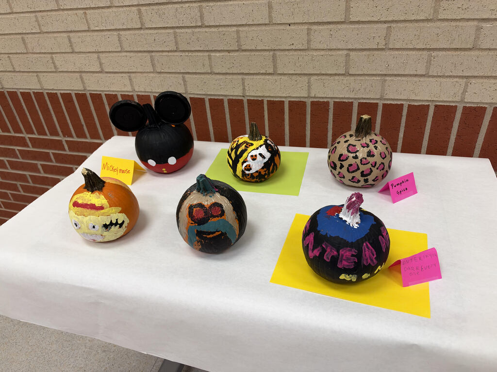 A table displaying several creatively decorated and painted pumpkins, including designs shaped like Mickey Mouse, animal prints, and colorful patterns.