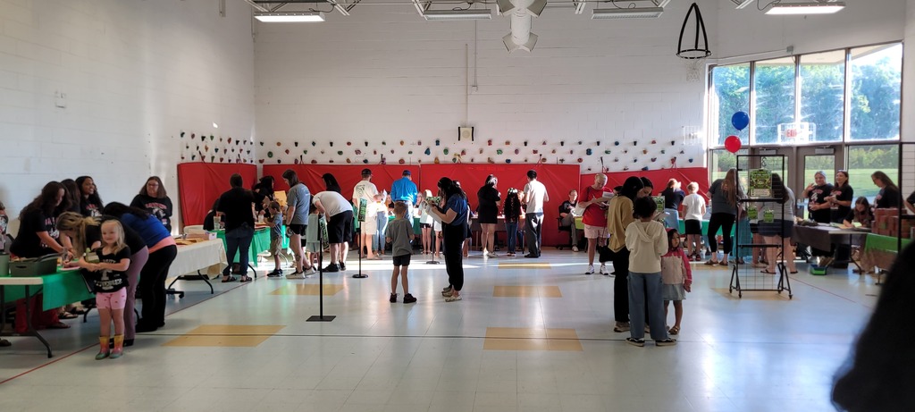 An indoor hall with tables, people, and a red wall. Tables have items on them.