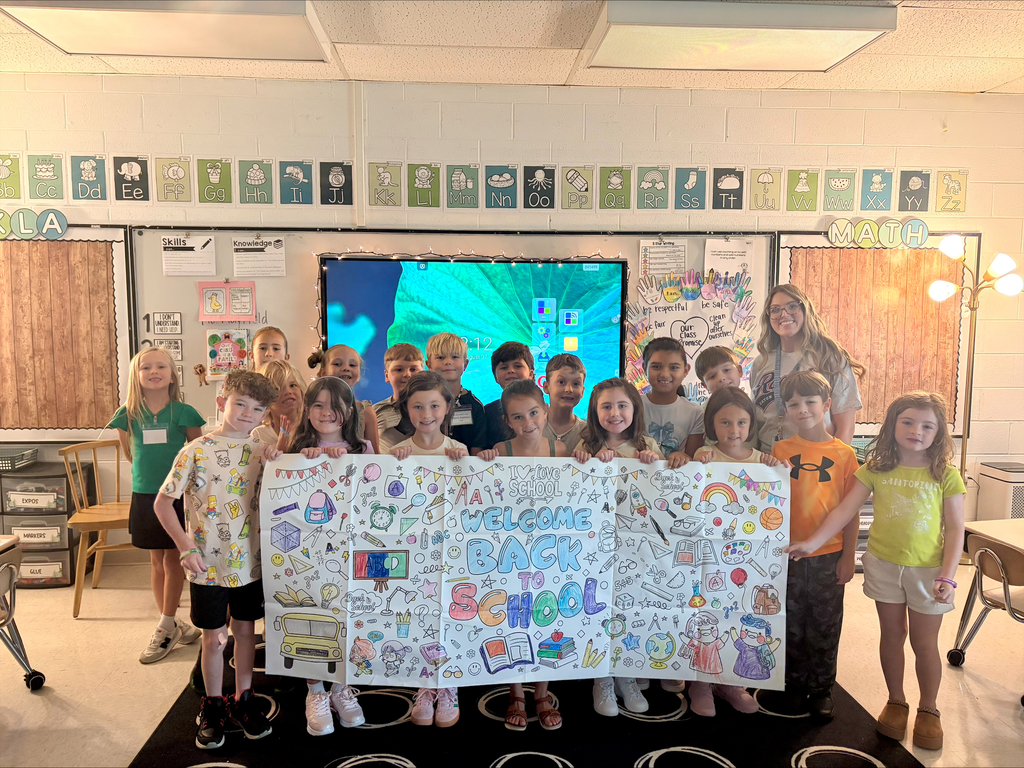 Classroom with students and a teacher; students holding a colorful banner reading "Welcome Back School."