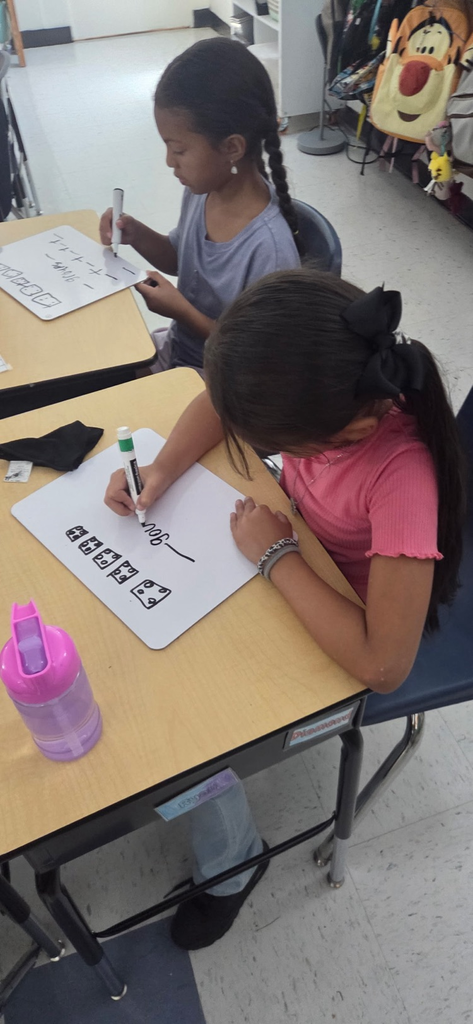 two girls writing on white boards to solve multiplication problems