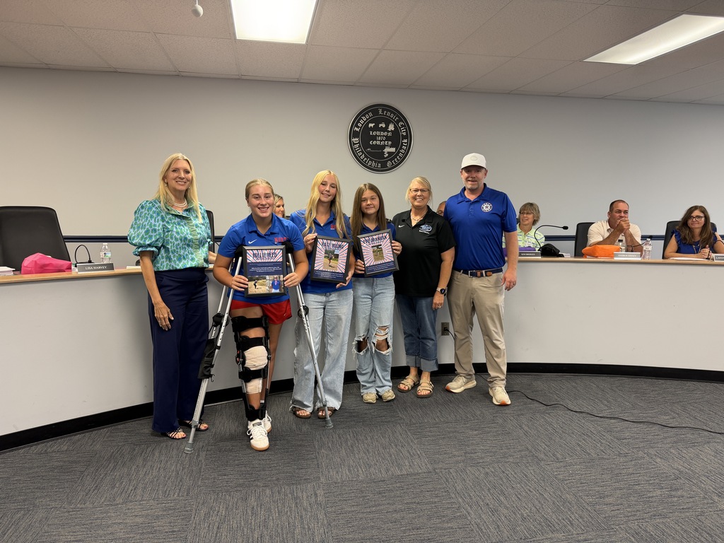 Five adults stand in a conference room. One has a cast on their right leg. They hold certificates.