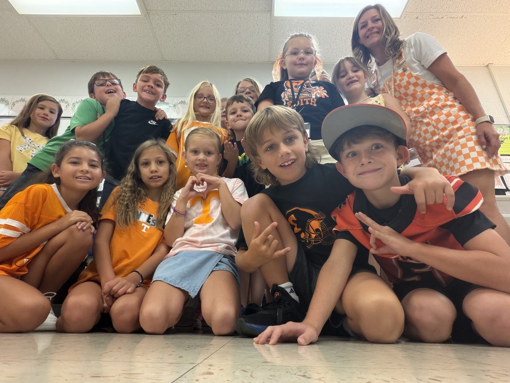 Group of kids in various sports jerseys and casual clothes, sitting and standing, posing for a photo.