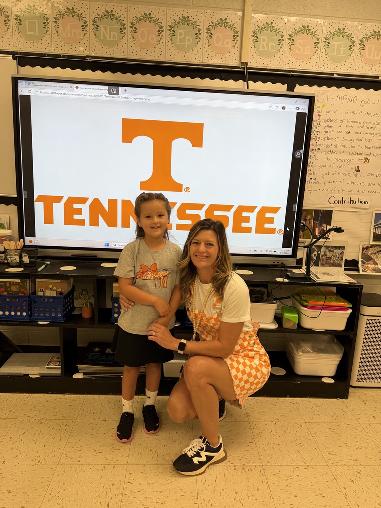 Woman kneeling next to a child in front of a classroom screen showing the letter T.