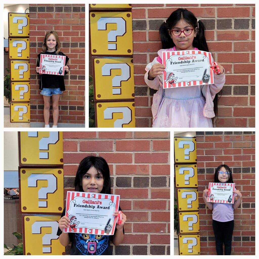 Four young girls holding certificates, smiling. They stand against a brick wall with yellow question mark signs.