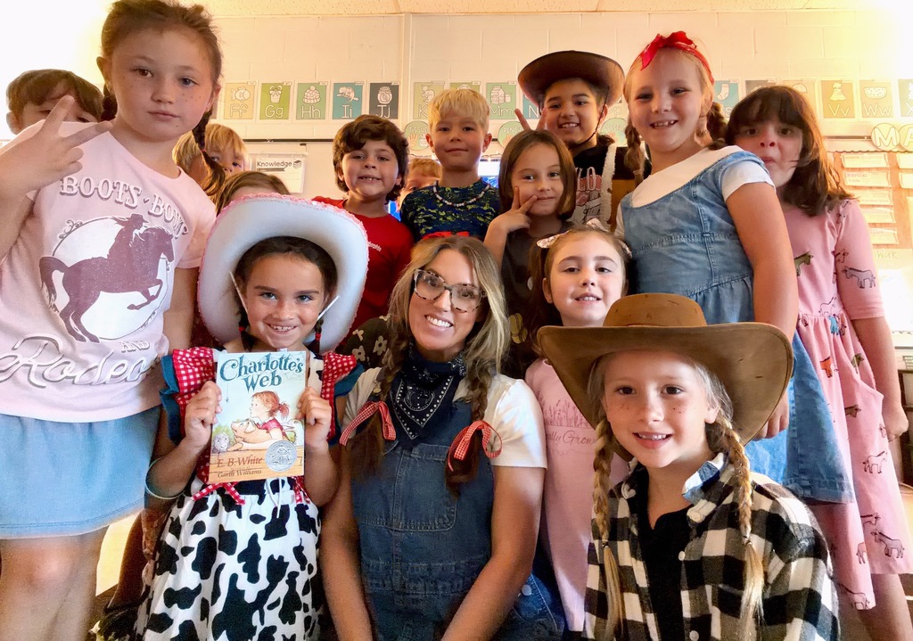 Children and a woman pose together for a photo in a classroom. Some wear hats and costumes.