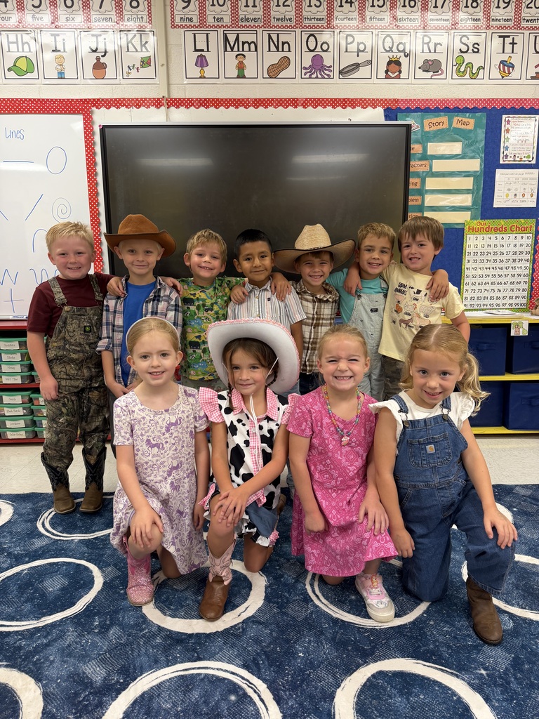 Kids dressed in cowboy costumes pose for a group photo in a classroom with a whiteboard.