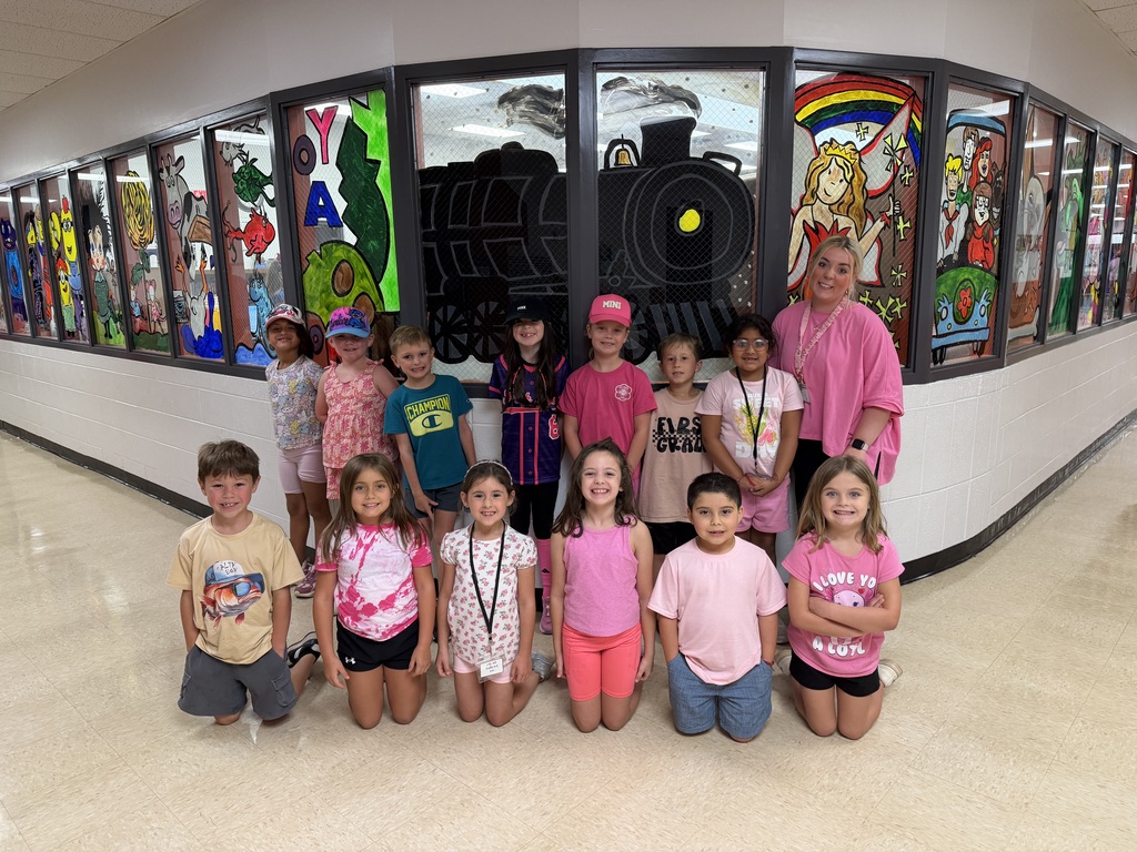 A group of children poses in front of a wall with colorful glass art in a hallway.