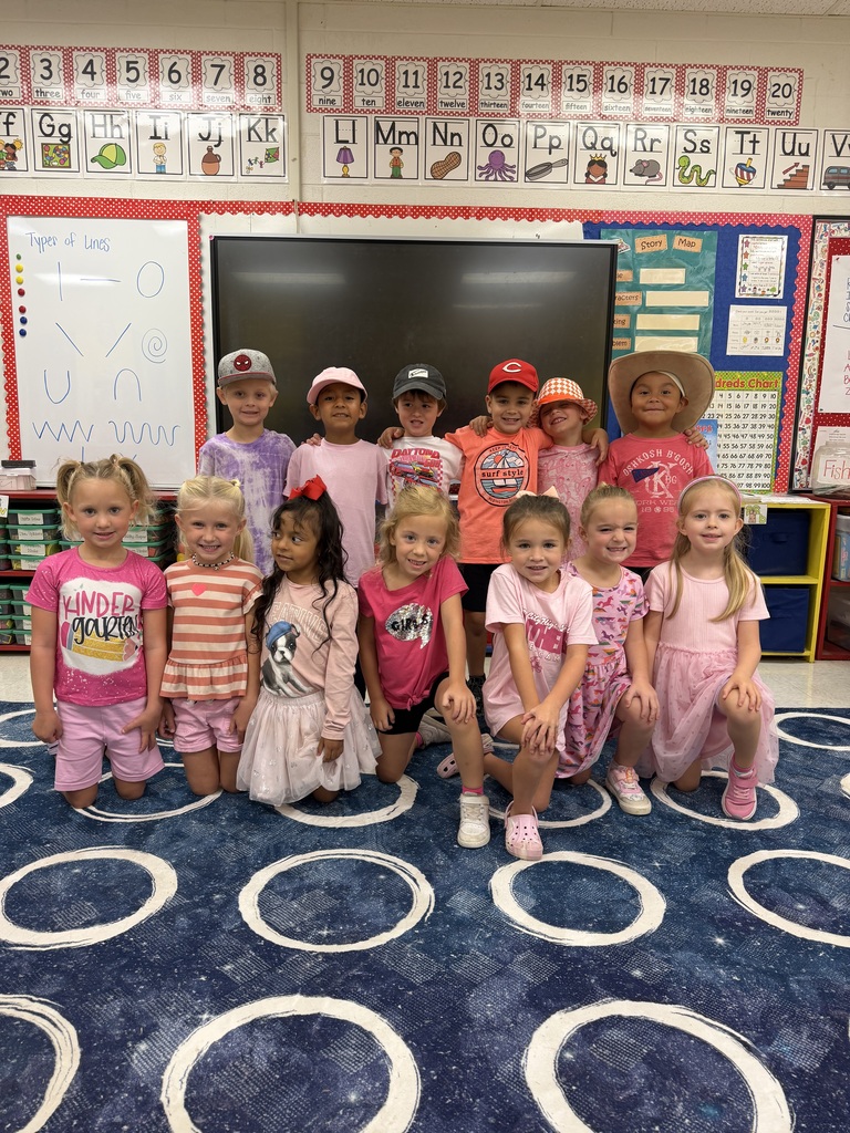 A group of children, aged 4-6, stand in a classroom. They wear different outfits and pose for a photo.