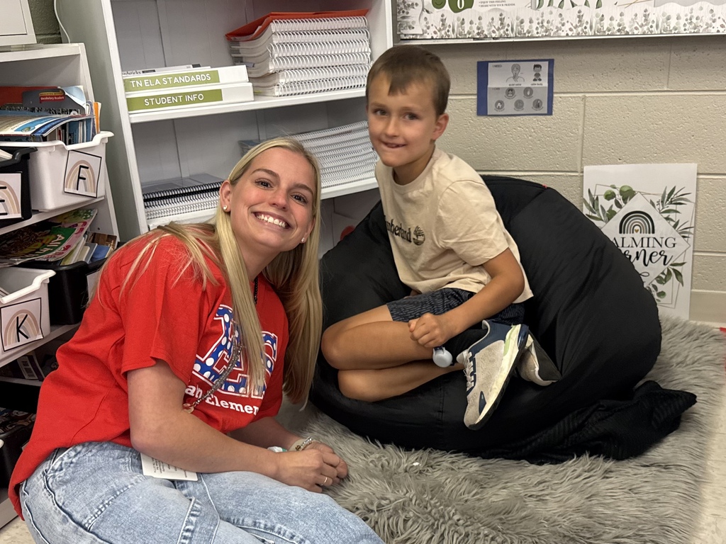 Woman in red shirt and denim jeans sitting on the floor next to a boy in shorts.