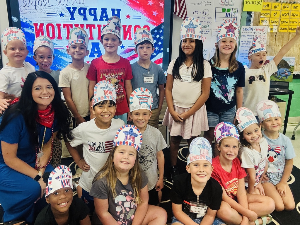 A group of children and an adult in a classroom, some wearing patriotic hats, smiling for a picture.