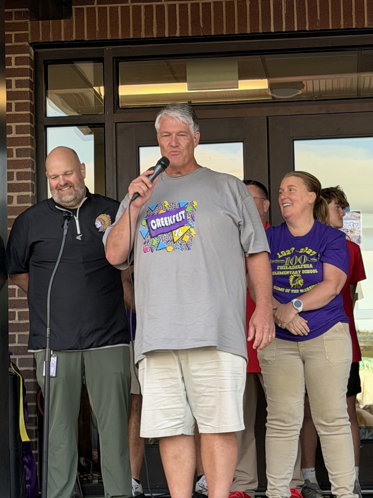 Man holds microphone near podium, speaking to crowd; others stand behind him, looking on.