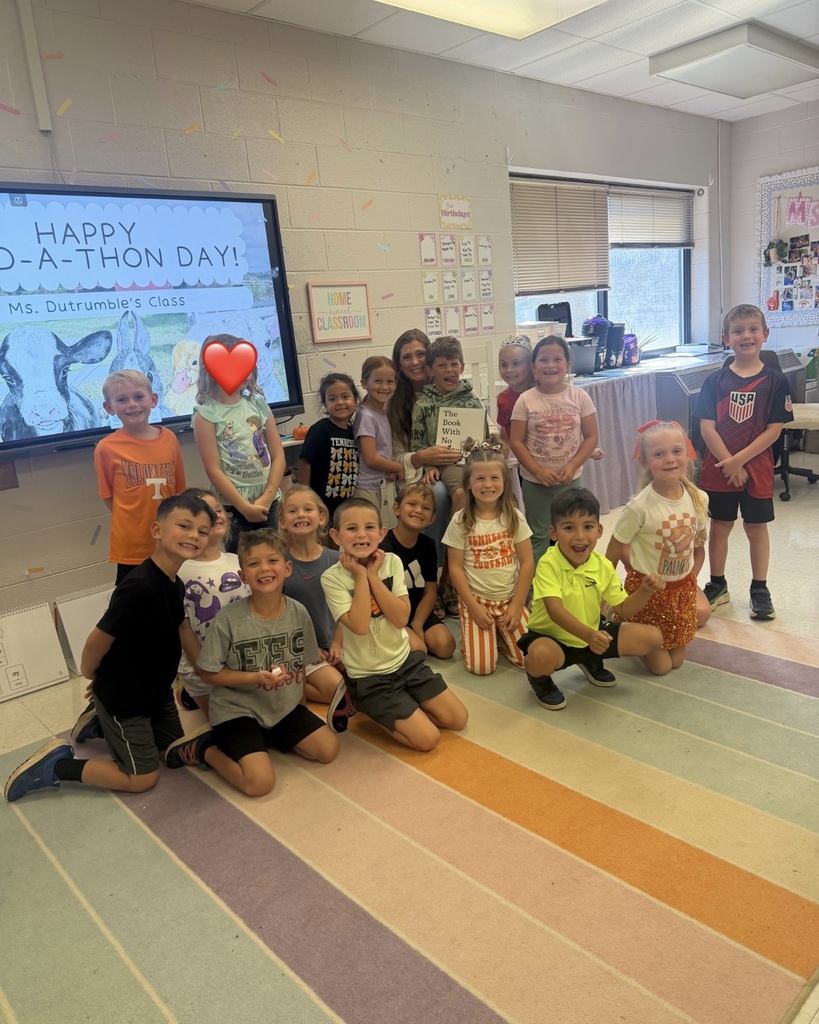 Kids pose for a group photo in a classroom, with a large screen displaying a message.