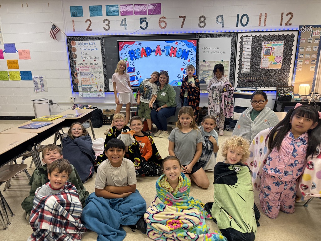 Children and adults in pajamas and blankets pose for a group photo in a classroom.
