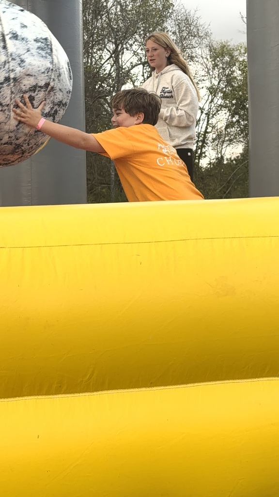 Two children playing on a yellow inflatable. One boy in orange is pushing a large black and white ball.
