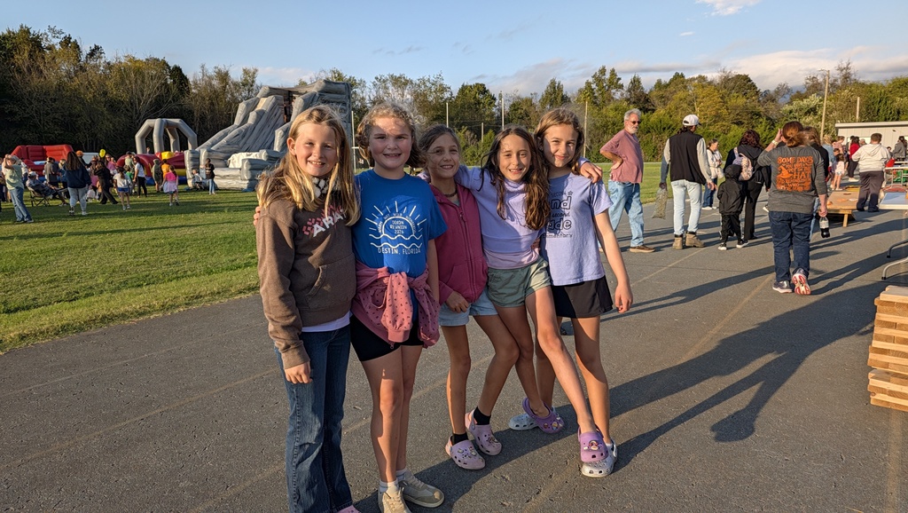Five girls in casual attire posing on a paved path near an inflatable playground.