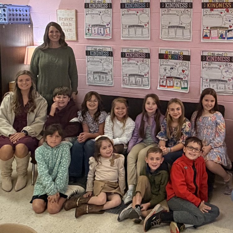 A group of young children and two adults pose for a picture in a classroom.