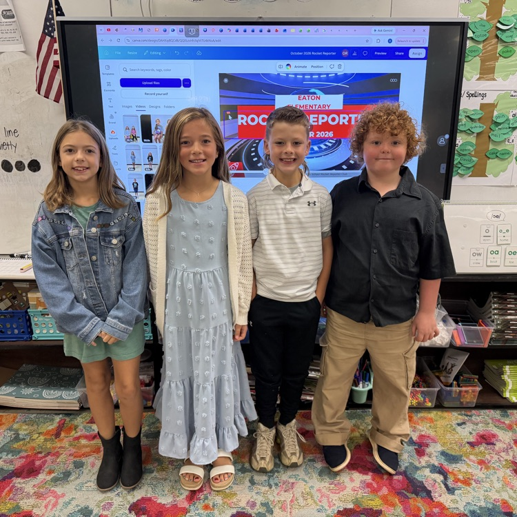 Four children stand in front of a classroom screen with a sports event on it.