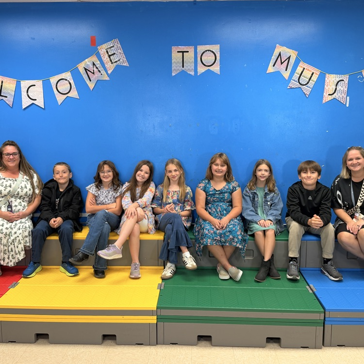 Students and staff seated on colorful steps; a blue wall has a banner that reads "Welcome to Music".