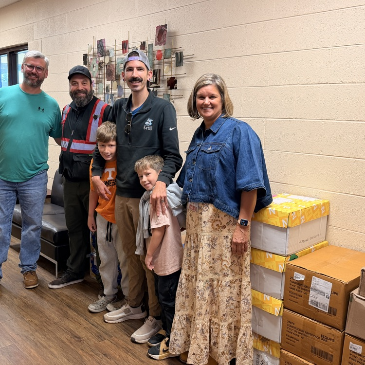 People pose for a photo near a stack of cardboard boxes with several children and adults.